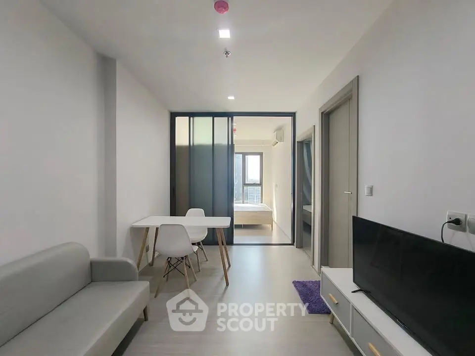 Modern apartment interior with open living and dining area leading to a bedroom.