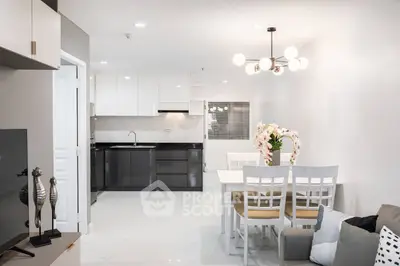 Modern open-plan living space with sleek white tiles, featuring a well-equipped kitchen with dark cabinetry and a cozy dining area.