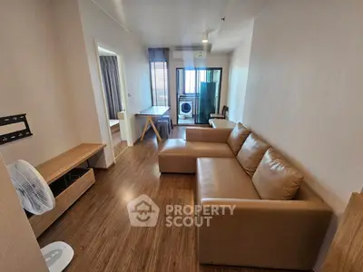 Modern living room with brown leather sofa and wooden flooring, featuring a washing machine in the background.