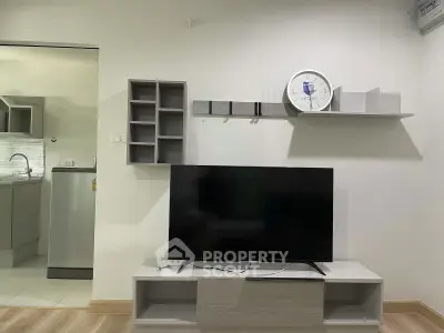 Modern living room with sleek TV stand and wall-mounted shelves, adjacent to a compact kitchen area.
