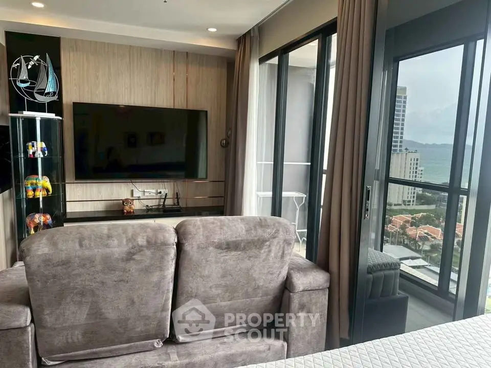 Modern living room with plush sofa, large TV, and stunning balcony view of cityscape.