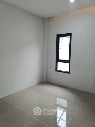 Spacious empty room with tiled flooring and a large window, perfect for customization.
