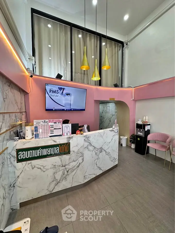 Modern reception area with marble counter and pink accents, featuring high ceilings and stylish lighting.