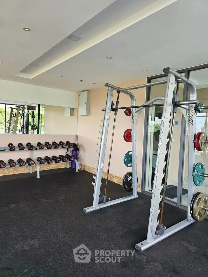 Modern gym with weightlifting equipment and mirrored walls in a luxury apartment complex.
