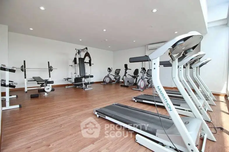 Spacious modern gym with state-of-the-art fitness equipment and wooden flooring in a luxury residential building.