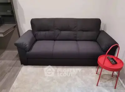 Cozy living room with dark sofa and vibrant red side table on plush carpet.