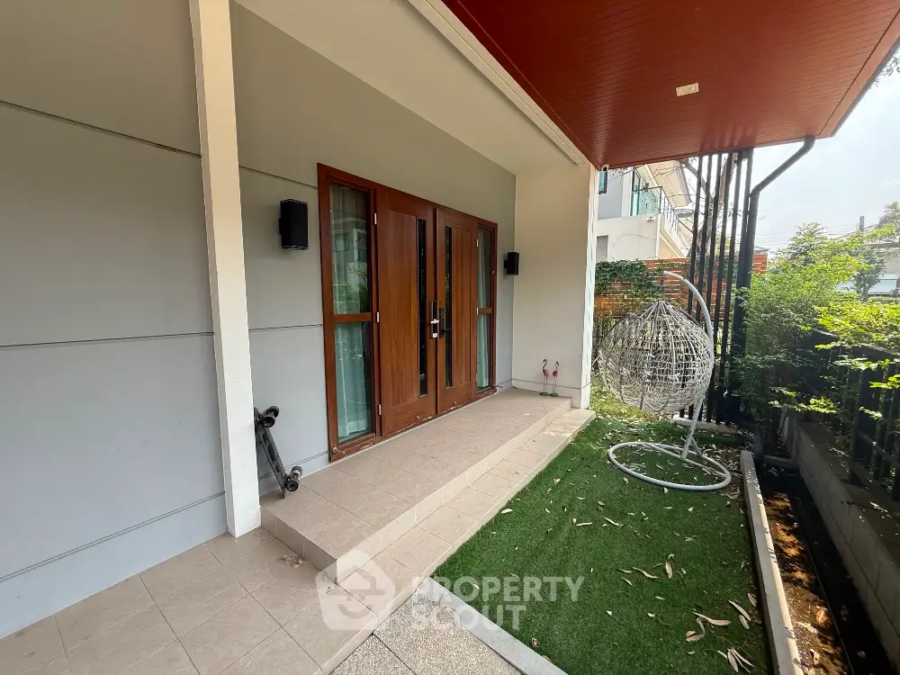 Modern home entrance with stylish hanging chair and lush greenery