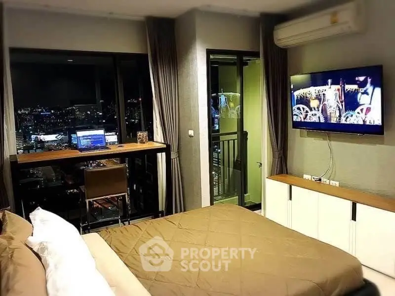 Modern bedroom with city view, wall-mounted TV, and workspace in luxury apartment.
