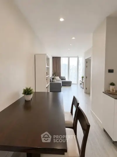 Modern open-plan living room with dining area and city view, featuring sleek furniture and natural light.