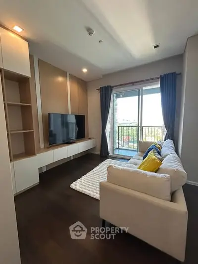 Modern living room with large TV and balcony view, featuring stylish decor and comfortable seating.