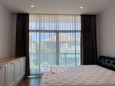 Spacious bedroom with large window and elegant curtains, offering a serene view of the outdoors.