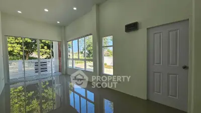 Spacious living room with large windows and glossy floors, offering abundant natural light and garden view.