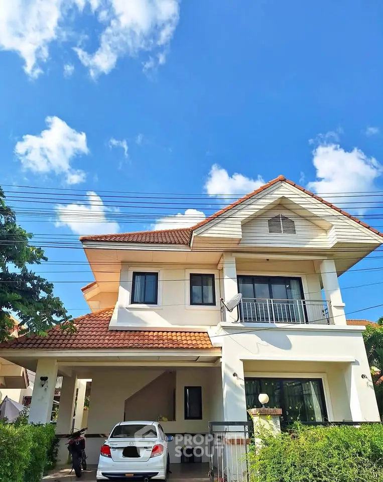 Charming two-story house with a red-tiled roof and lush greenery under a clear blue sky.