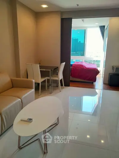 Modern apartment with open living room and bedroom view, featuring sleek furniture and cityscape window.