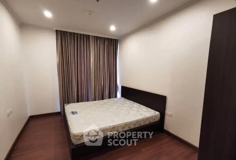 Spacious bedroom with wooden flooring and large window with curtains in modern apartment.