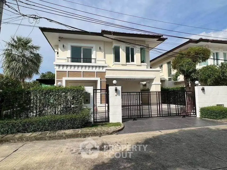 Elegant two-story house with gated entrance and lush greenery in a serene neighborhood.