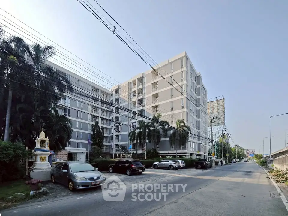 Modern apartment building with parking and lush greenery on a sunny day.