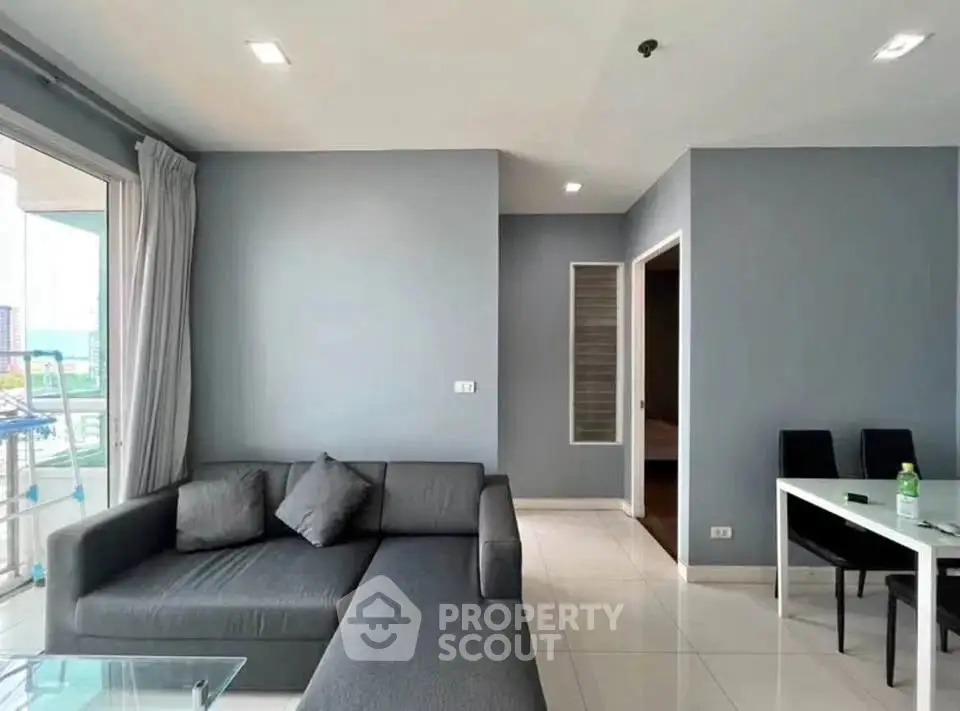 Modern living room with sleek gray sofa and dining area in open layout apartment.