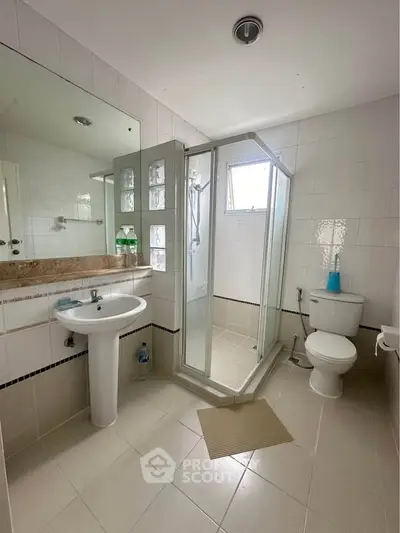 Modern bathroom with glass shower and white fixtures in spacious apartment