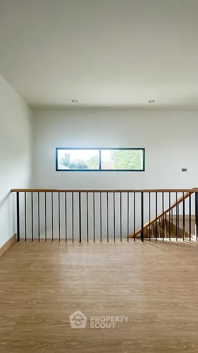 Bright stairway with wooden flooring and modern railing, featuring a large window view.