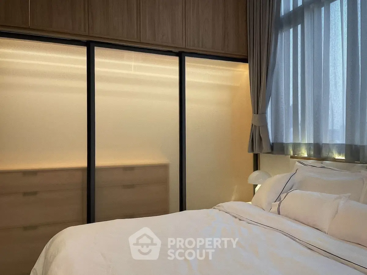 Elegant bedroom with soft lighting and large window, featuring modern built-in wardrobes and cozy bedding.