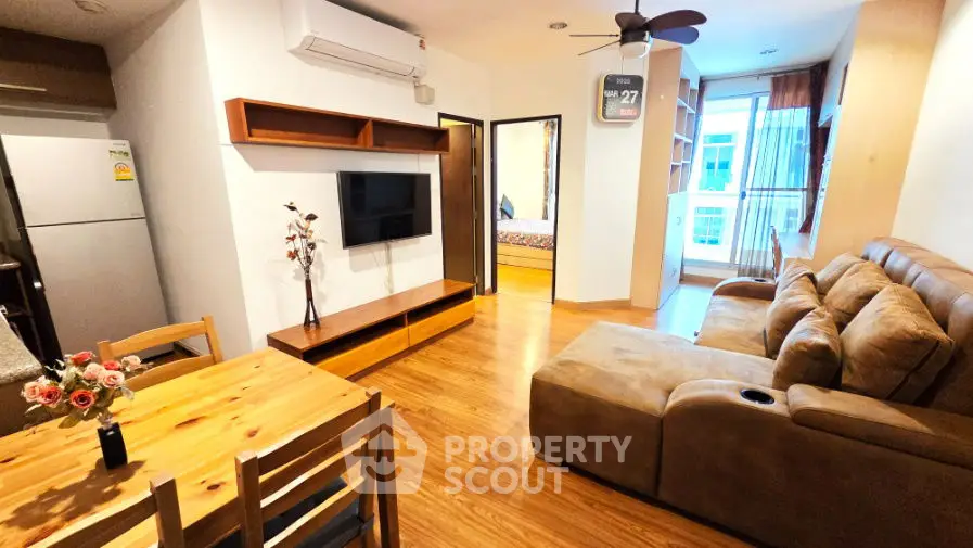 Modern living room with cozy sofa and wooden flooring, adjacent to dining area and visible bedroom.