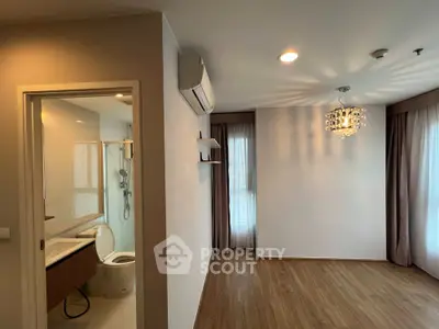 Spacious and well-lit corner unit with elegant chandelier, large windows with curtains, and a peek into the modern bathroom.