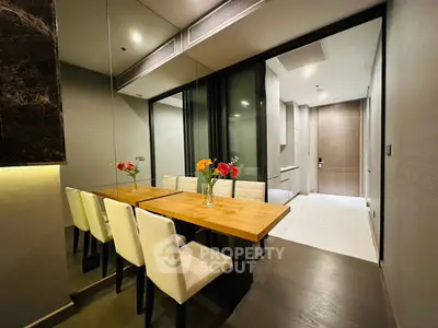 Modern dining area with elegant wooden table and white chairs, adjacent to sleek kitchen in luxury apartment.