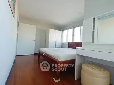 Spacious bedroom with wooden flooring and ample natural light, featuring a comfortable bed and elegant wardrobe.