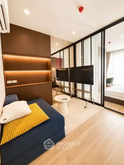 Modern living room with stylish decor and glass partition leading to bedroom, featuring cozy seating and wooden flooring.