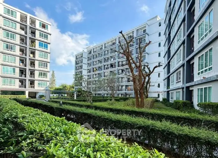 Modern apartment complex with lush green garden and clear blue sky.