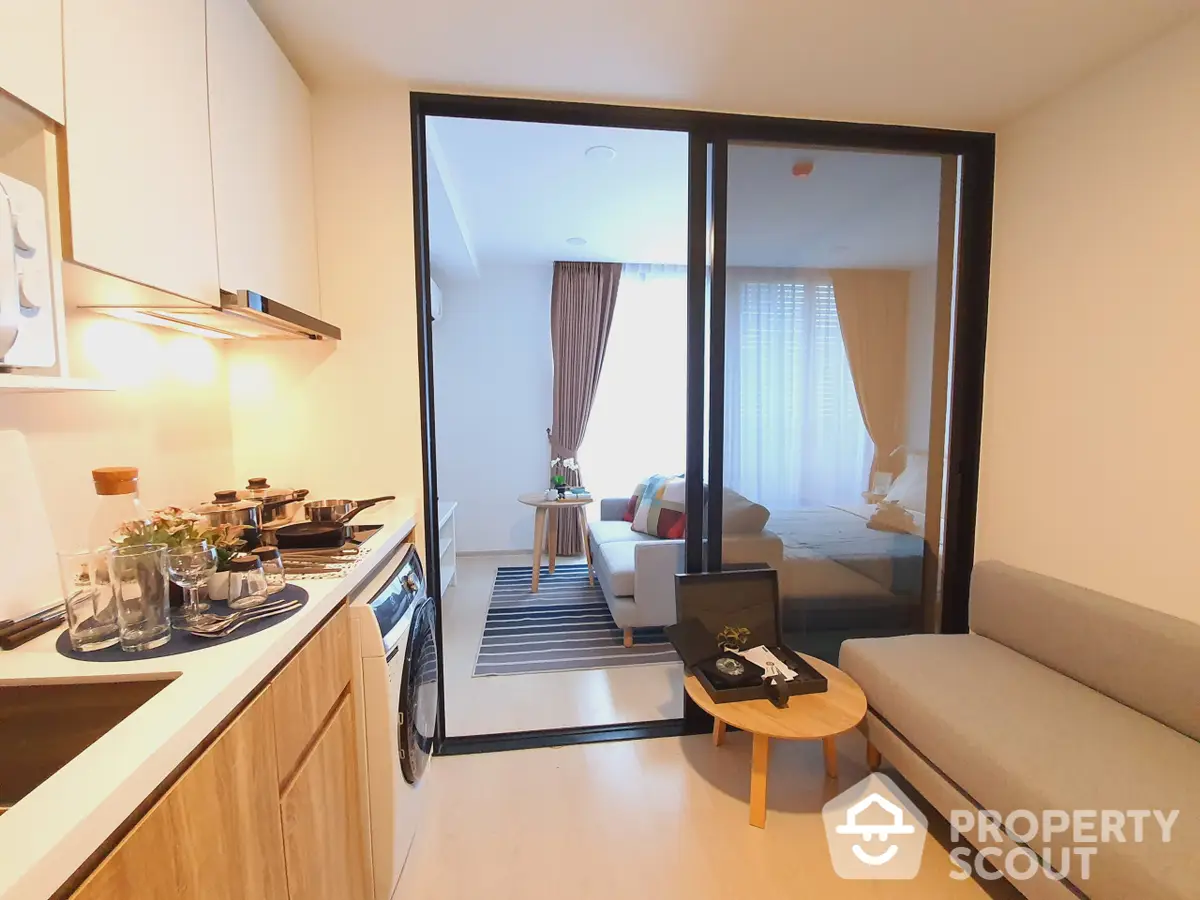 Modern studio apartment with seamless open layout integrating a stylish kitchen, cozy living space, and a welcoming bedroom area behind sliding glass doors.