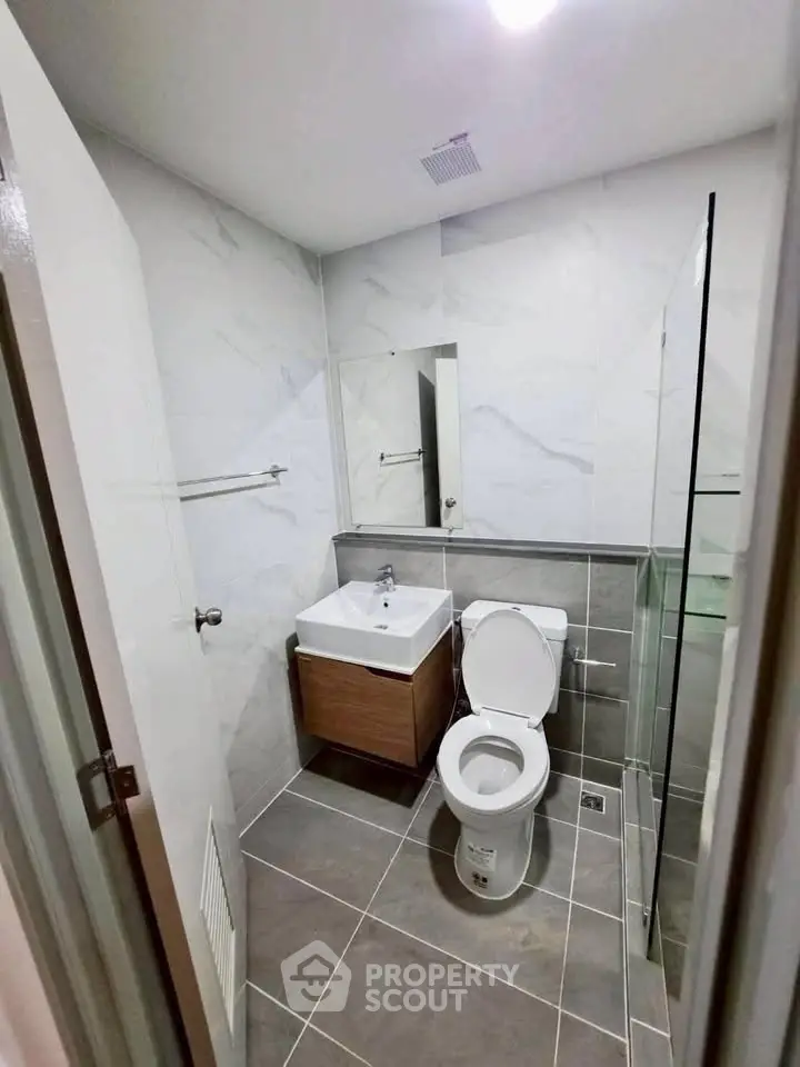 Modern bathroom with sleek design, featuring a white toilet, sink, and glass shower enclosure.