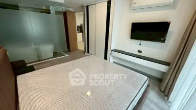 Modern bedroom with glass partition and wall-mounted TV in stylish apartment.