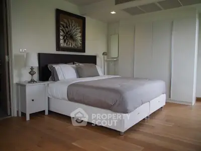 Modern bedroom with elegant decor and wooden flooring, featuring a cozy bed and stylish artwork.