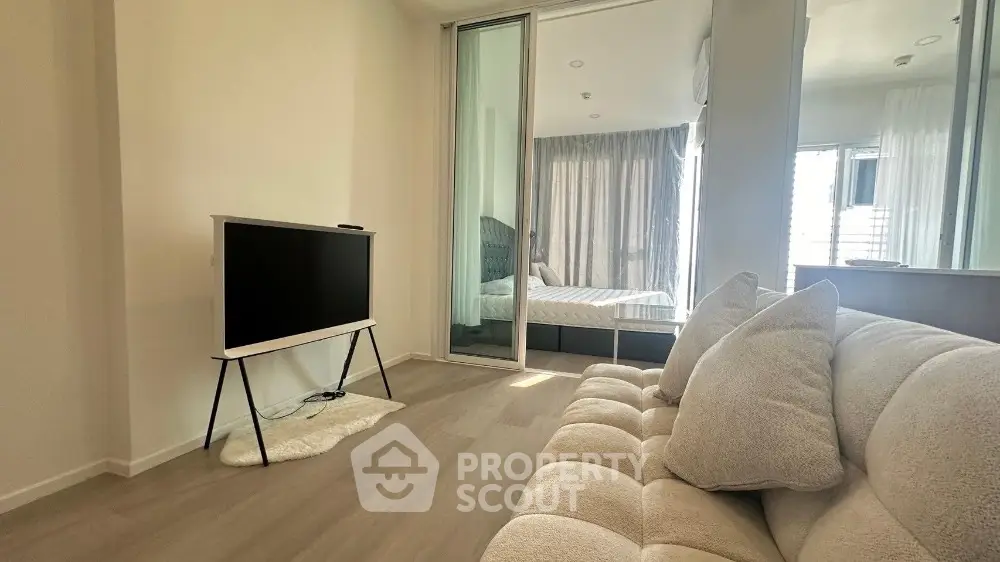 Modern living room with cozy sofa and TV, leading to a stylish bedroom with natural light.