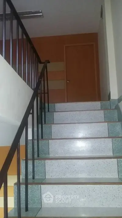 Well-maintained staircase with terrazzo flooring leading to a warm wooden door, showcasing the property's secure and accessible design.