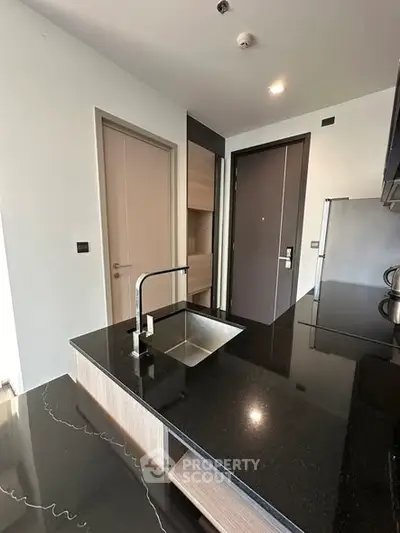 Modern kitchen with sleek black countertops and stainless steel sink in a contemporary apartment.