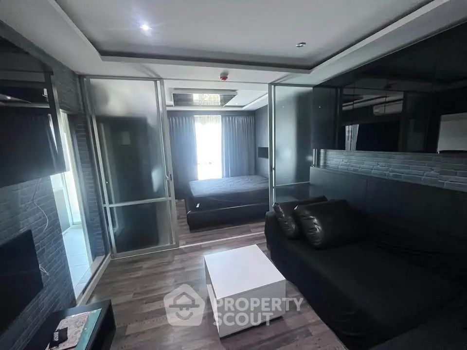 Modern studio apartment with sleek black furnishings and glass partitions, featuring a cozy living area and bedroom.