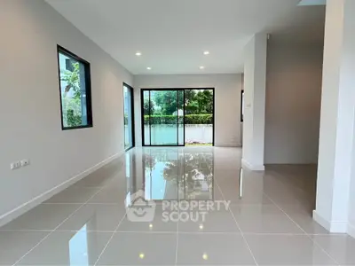 Spacious modern living room with glossy tiled floors and large windows offering serene garden views.