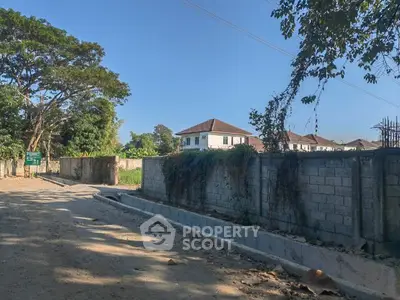 Expansive vacant land ready for development, surrounded by a secure wall and mature trees, near a serene residential area.