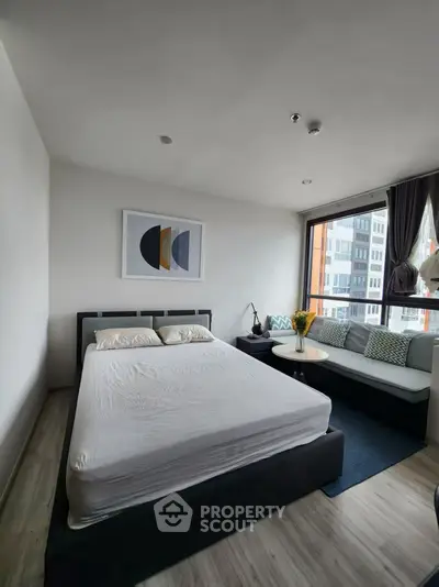 Modern bedroom with large window and stylish decor in urban apartment.