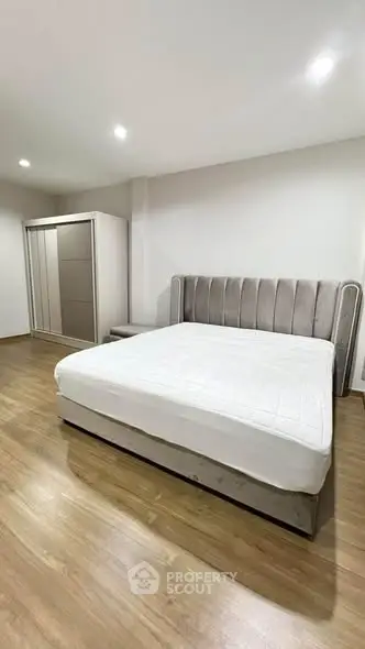 Spacious bedroom with modern bed and wardrobe, featuring sleek wooden flooring.