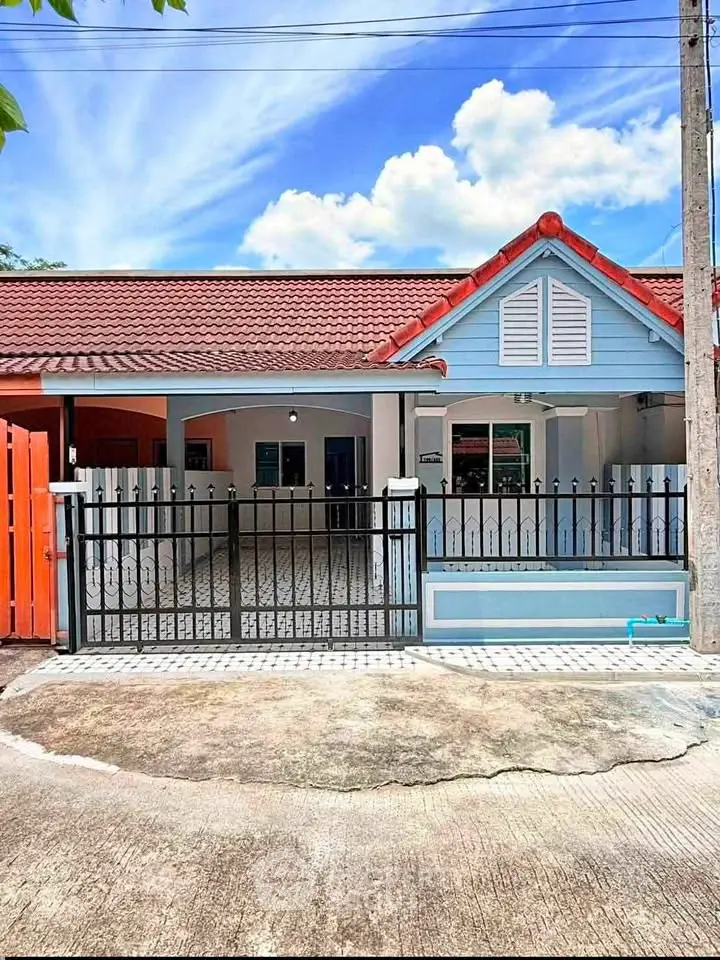 Charming single-story home with red roof and blue facade, featuring a gated driveway and inviting front porch.