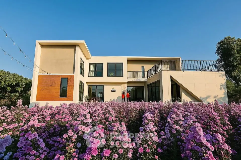 Modern two-story house with large windows and beautiful flower garden under clear blue sky.