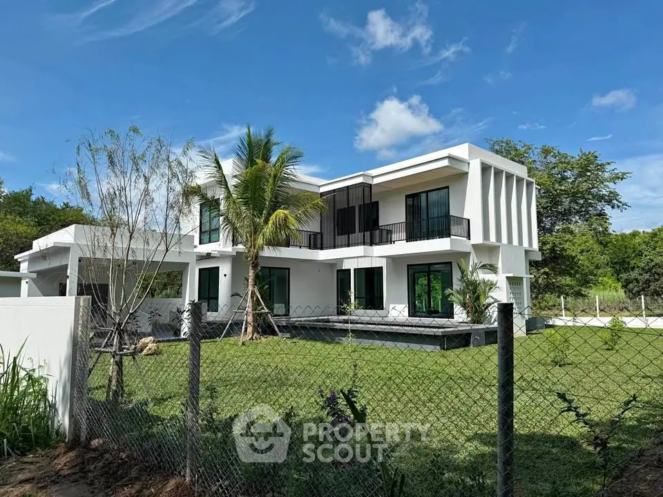Modern two-story white house with lush garden and palm tree, showcasing contemporary architecture.
