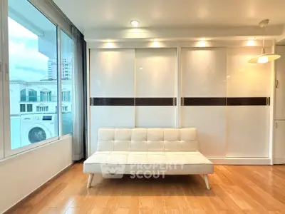 Modern living room with sleek white furniture and large windows offering city views.