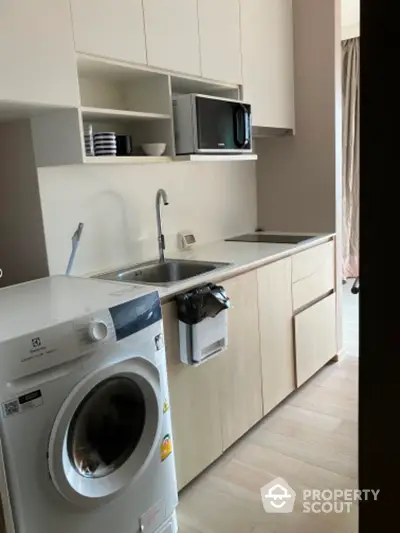 Modern compact kitchen with washing machine and microwave in sleek apartment