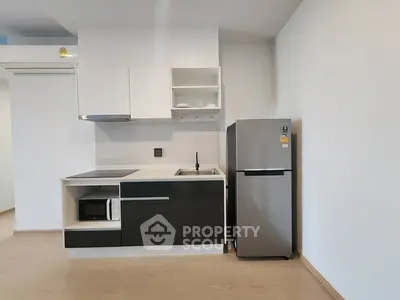 Modern kitchen with sleek cabinetry, microwave, and stainless steel fridge in minimalist design.