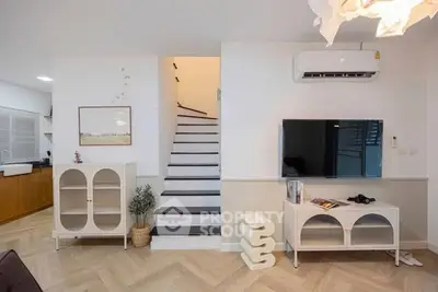 Modern living room with stylish furniture and staircase, featuring air conditioning and contemporary decor.